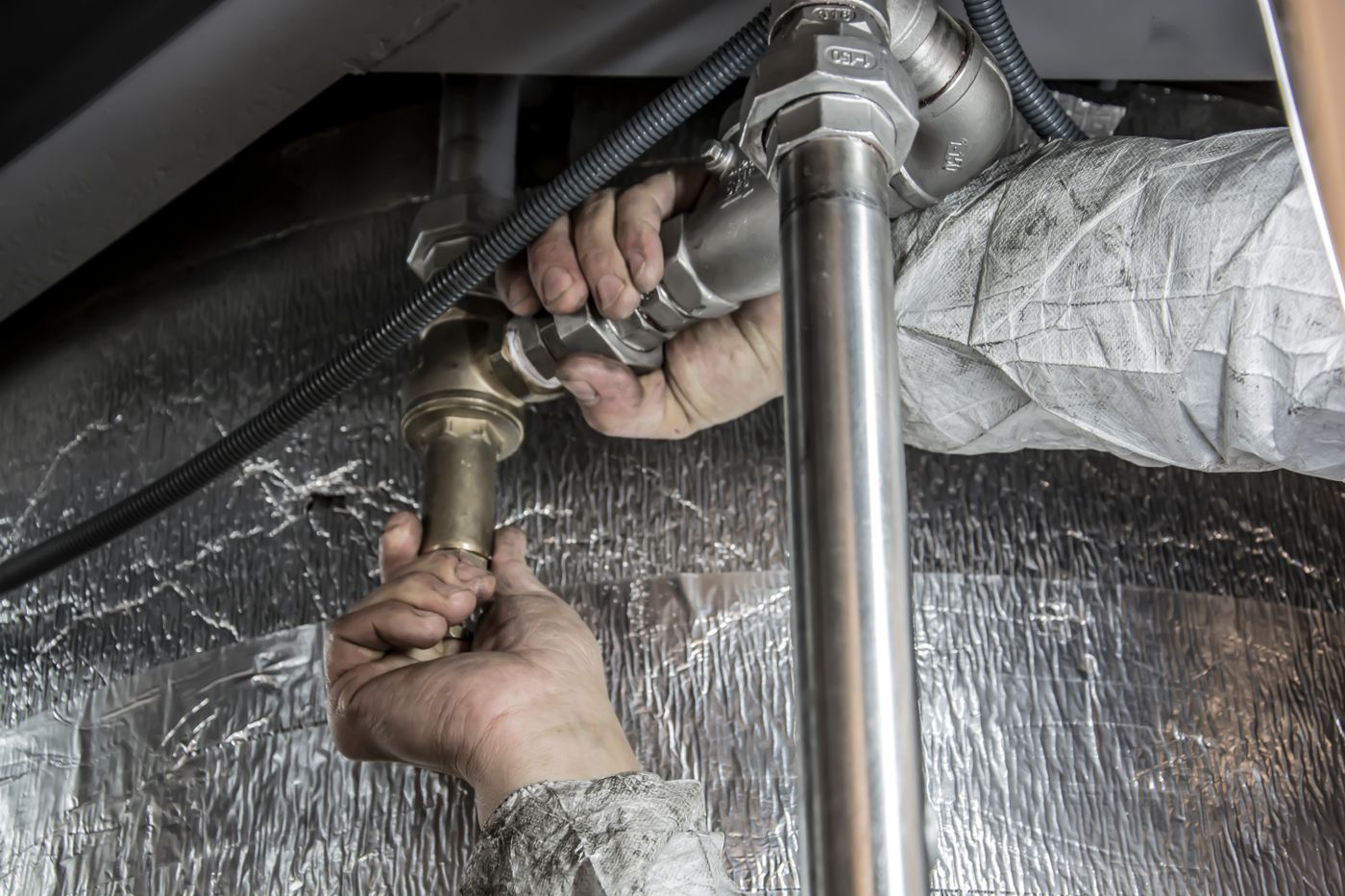Installateur verschraubt Rohrleitungen unter einer Anlage