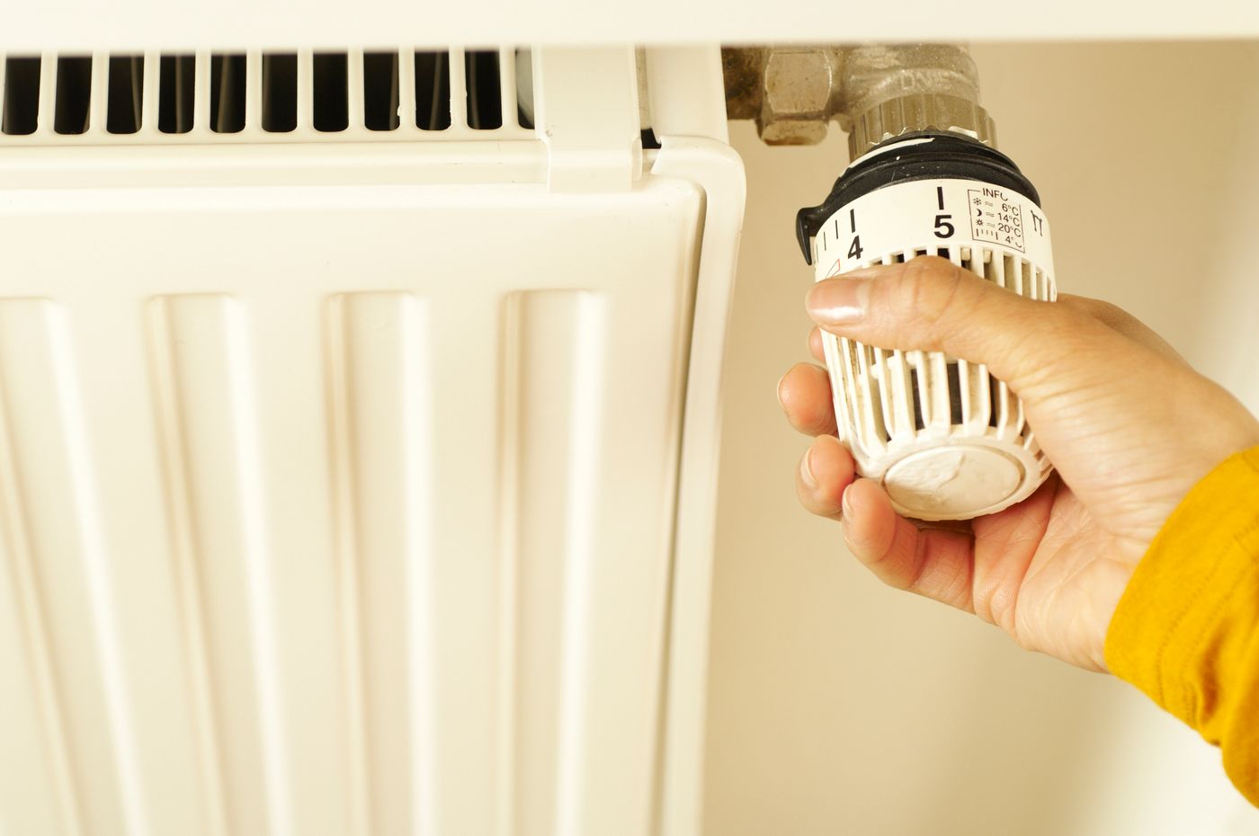 Hand stellt ein Heizkörper-Thermostat ein